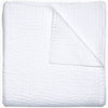 A Vivada White Woven Quilt by John Robshaw folded on top of a white surface with hand stitching.