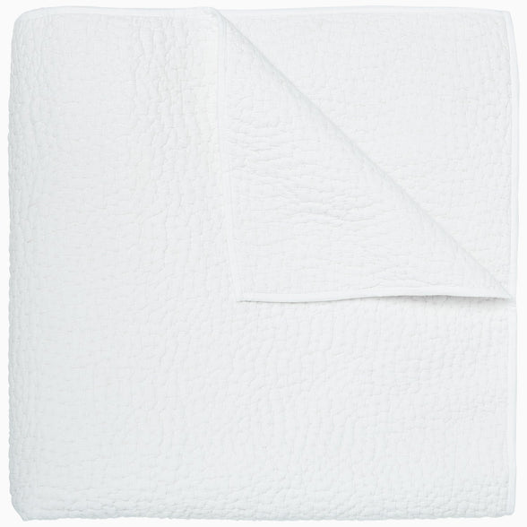 An Organic Hand Stitched White Quilt by John Robshaw folded on top of a white surface.