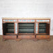 The Gulab Side Board by John Robshaw is a vintage teak sideboard featuring three open cabinet doors and three drawers below, adorned with a painted floral design along the upper front and accented by elegant floral tile insets for added charm.