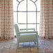 A Square Chair in Aleppo Sage by John Robshaw sits on a tiled floor in front of a large arched window with patterned curtains, its custom Aleppo Sage Performance Fabric upholstery adding an elegant touch to the serene space.