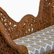 The Candra Teak Sofa by John Robshaw features an ornately carved wooden frame with an intricate floral pattern on the backrest and a cushioned seat upholstered in blue and yellow floral fabric, beautifully capturing the vintage charm of Anglo Indian furniture.