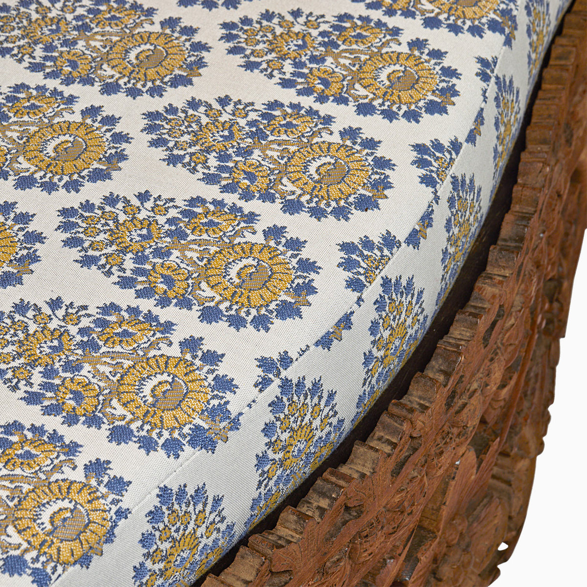 Close-up of a cushion with blue and yellow floral patterns on the Candra Teak Sofa by John Robshaw.
