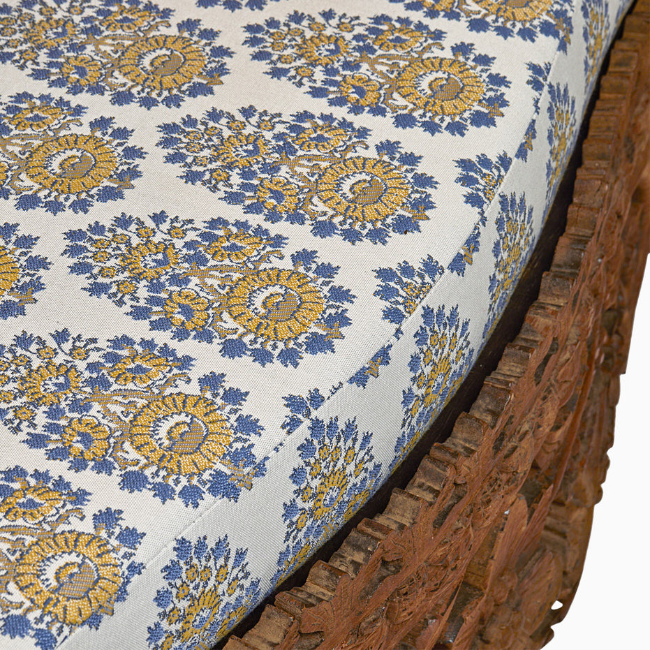 Close-up of a cushion with blue and yellow floral patterns on the Candra Teak Sofa by John Robshaw.
