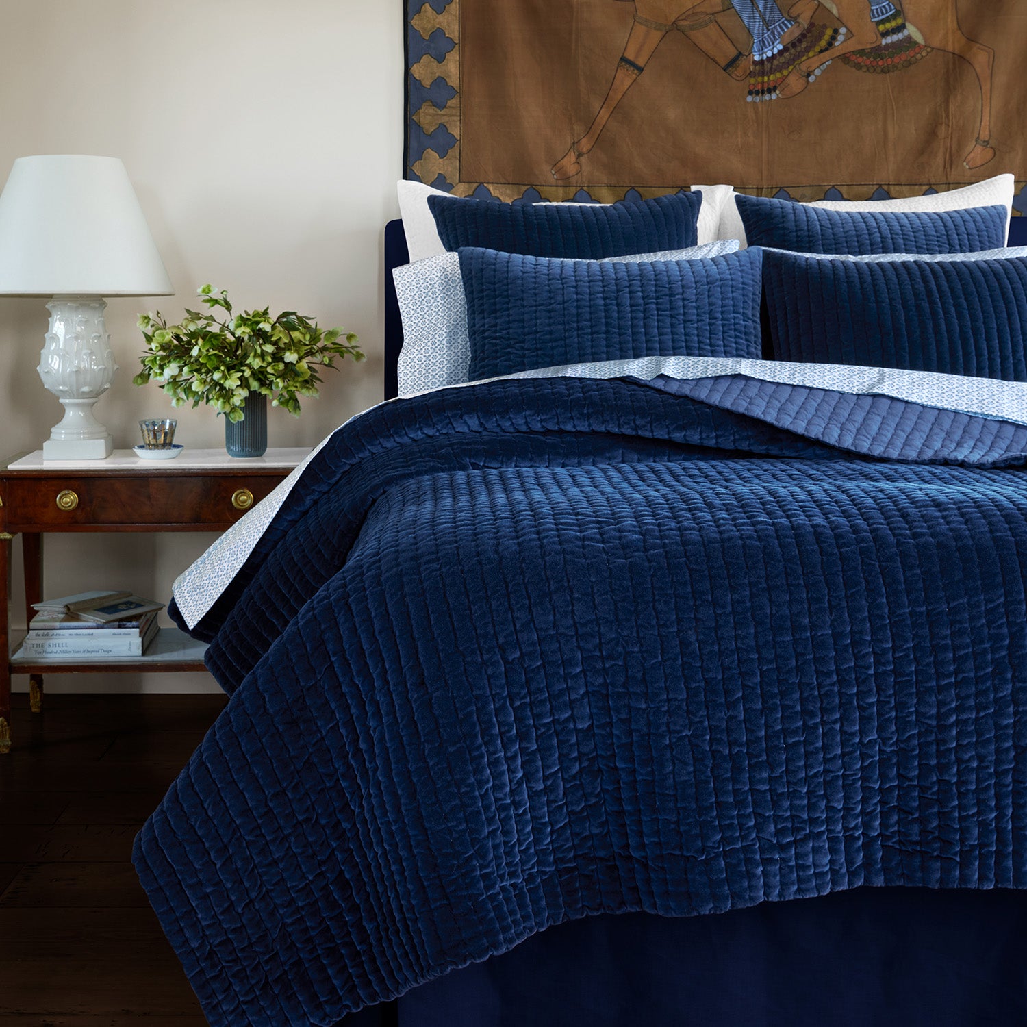 A John Robshaw Velvet Indigo Quilt with a blue velvet comforter and pillows, crafted by Indian artisans.