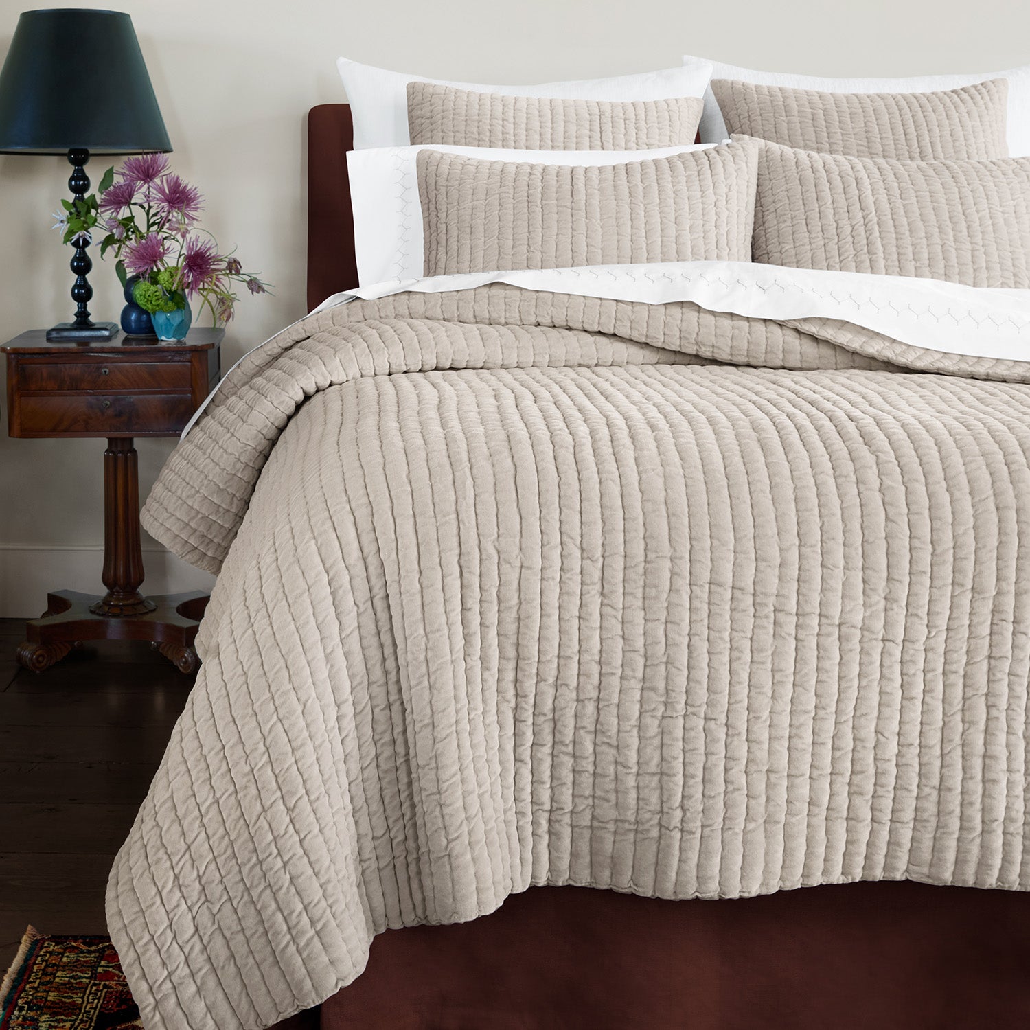 A soft bed with a John Robshaw beige Velvet Sand Quilt and plush pillows.