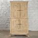 The Capala Teak 2 Part Cabinet by John Robshaw is a tall, rustic piece crafted from bleached teak, featuring paneled doors and metal handles. With its two main sections and refined design, this cabinet stands beautifully against a white brick wall on a concrete floor—a perfect choice for vintage furniture enthusiasts.