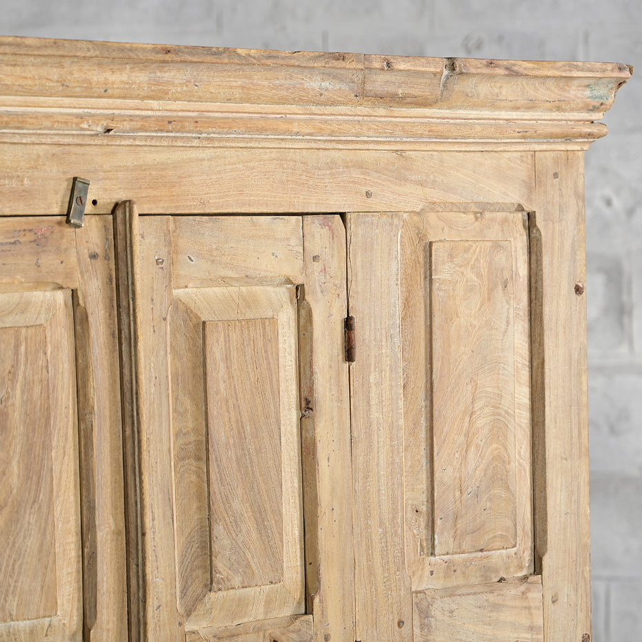 Close-up of the top section of the John Robshaw Capala Teak 2 Part Cabinet, featuring bleached teak panels in a geometric design, set against a gray textured wall.