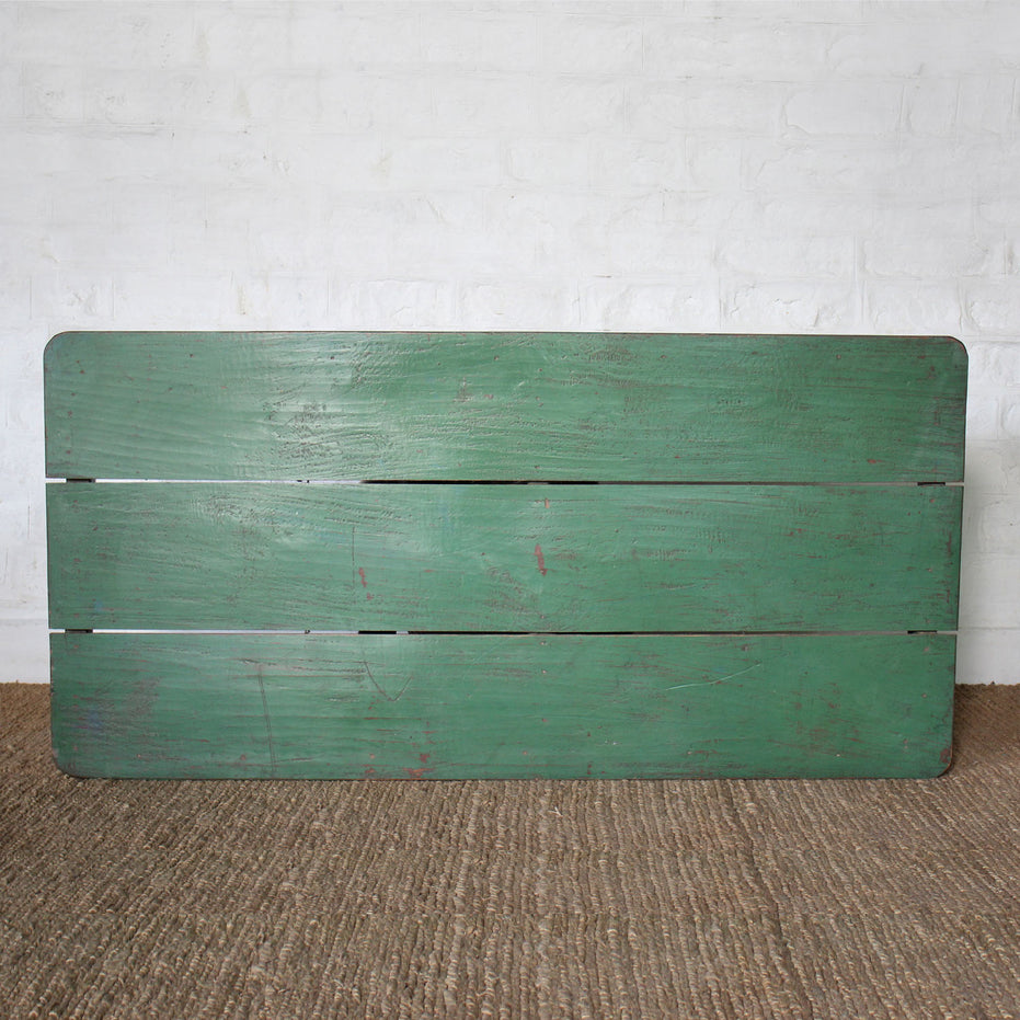 The Aangan Teak Coffee Table by John Robshaw features a plank-style top with three horizontal planks, set against a white brick wall and placed on a brown textured floor.