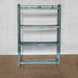 The Paarthiv Wooden Shelf by John Robshaw, with its distressed blue finish and subtle teal patina, stands against a white brick wall on a brown woven rug, exuding the timeless charm of vintage furniture.