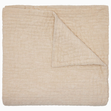 The Vivada Sand Woven Quilt by John Robshaw is shown here neatly folded with one corner turned over, highlighting the luxurious texture and substantial thickness of its cotton fabric—a refined addition to our reversible quilt collection, thoughtfully designed for comfort and style.