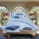 A bedroom with the John Robshaw Nandi Light Indigo Quilt, blue and white bedding, and pillows.