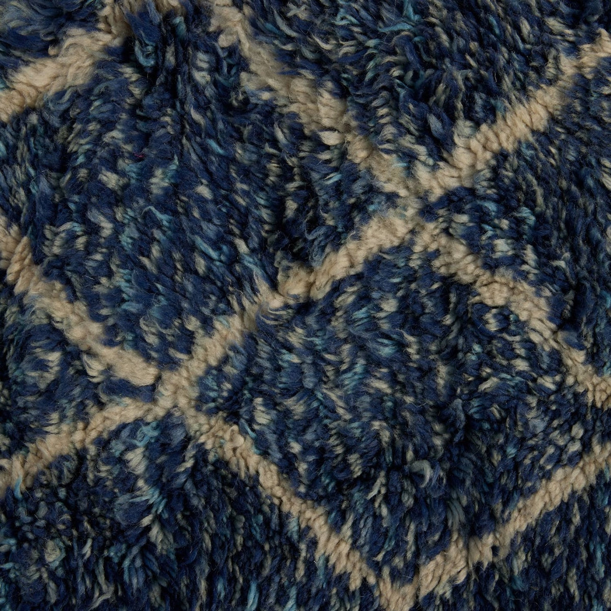 Close-up of a shaggy, handwoven John Robshaw Blue Village Wool Rug featuring a blue and white diamond pattern.