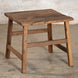 Introducing the Teak Side Table 7 by John Robshaw—a rustic, handcrafted teak side table featuring a rectangular top and four sturdy legs. Set against a light-colored brick wall on a concrete floor, this piece is perfect for those who appreciate the timeless charm of vintage-inspired furniture.