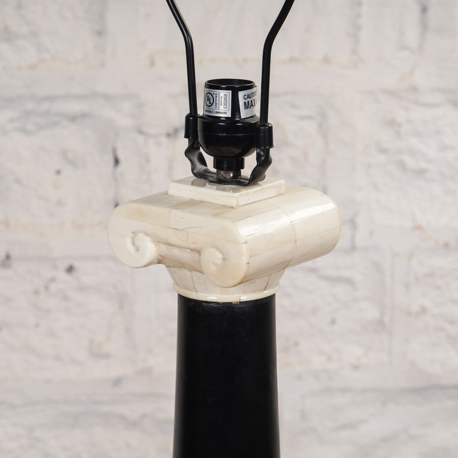 Close-up of the Roshni Bone Inlay Lamp by John Robshaw, featuring a design inspired by a classical column with a black base and a white Ionic capital, evoking the elegance of a Colonial Indian lamp, set against a light-colored textured wall.