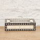 The Charita Bone Inlay Box by John Robshaw, featuring an intricate black and white striped pattern, is placed on a wooden surface against a white brick wall.