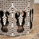 The Chandni Bone Inlay Table by John Robshaw features intricate geometric star and floral patterns delicately inlaid in white, reminiscent of traditional bone inlay craftsmanship, with striking arched cutouts along its sides, and is pictured here on a wooden floor.