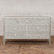 The Vajra Bone Inlay Sideboard by John Robshaw features a striking gray and white pattern with six drawers, adorned with decorative floral and geometric bone inlay, serving as a statement piece on a wooden floor against a white brick wall.