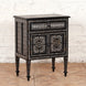 Introducing the Ahan Bone Inlay Cabinet by John Robshaw: a black wooden nightstand handcrafted to perfection, showcasing intricate white geometric inlay patterns. It features one drawer and two cabinet doors and stands elegantly on four tapered legs, pictured here against a white brick wall.