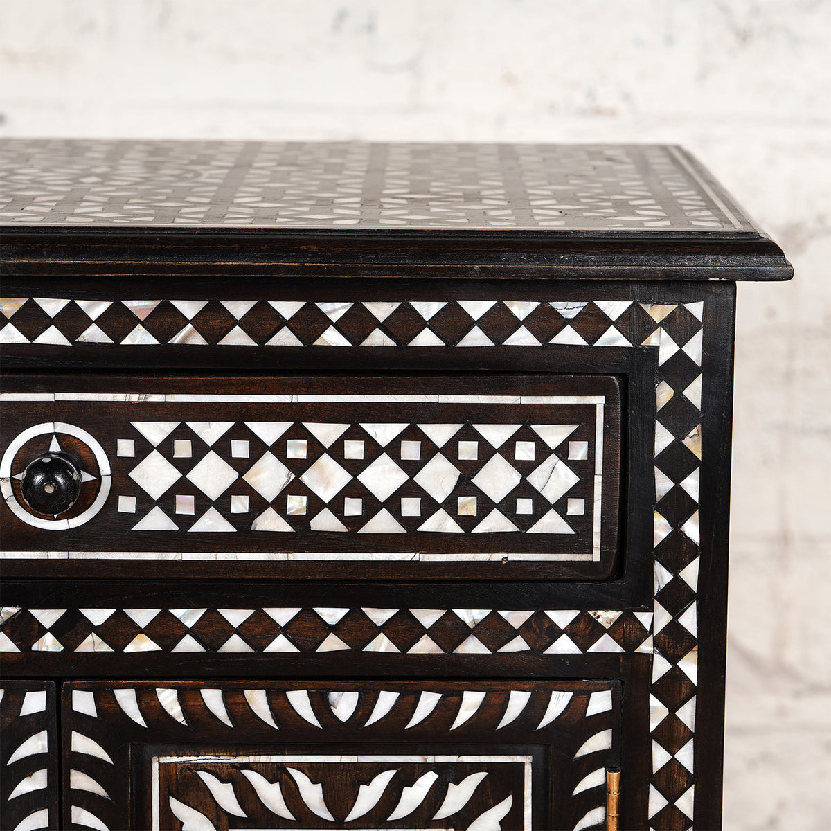 Close-up of the Ahan Bone Inlay Cabinet by John Robshaw, showcasing intricate white geometric patterns on its drawers and surface, set against a light-colored background.