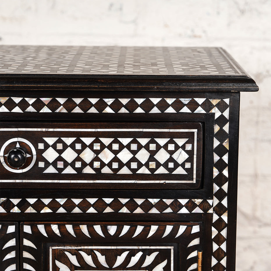 Close-up of the Ahan Bone Inlay Cabinet by John Robshaw, showcasing intricate white geometric patterns on its drawers and surface, set against a light-colored background.