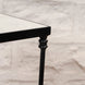 Close-up of a black metal leg with a decorative design on the John Robshaw Veda Side Table, supporting its rectangular tabletop against a light stone wall background, showcasing the minimalist elegance characteristic of this iron side table.