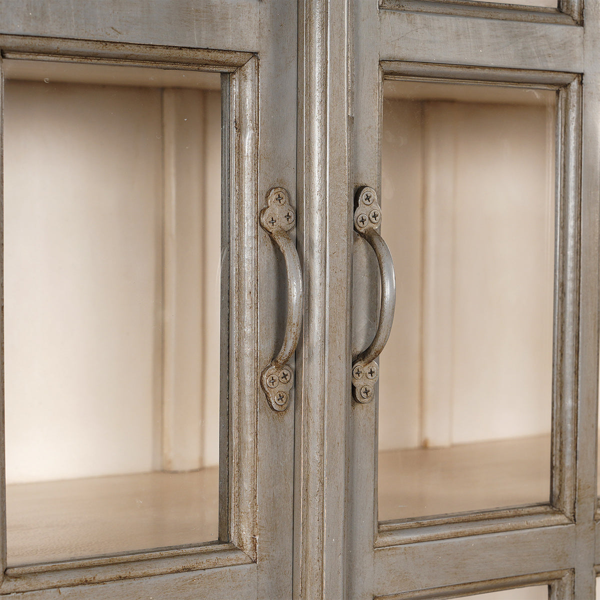 Close-up of two glass cabinet doors with metal handles and a distressed light gray painted wood frame, evoking vintage charm in the John Robshaw Kali Teak Cabinet.