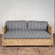 Experience vintage furniture at its finest with the Yashti Wooden Daybed by John Robshaw, featuring a carved wooden base and armrests, complemented by black and white block printed fabric seat and back cushions—beautifully set against a white brick wall on a wooden floor.