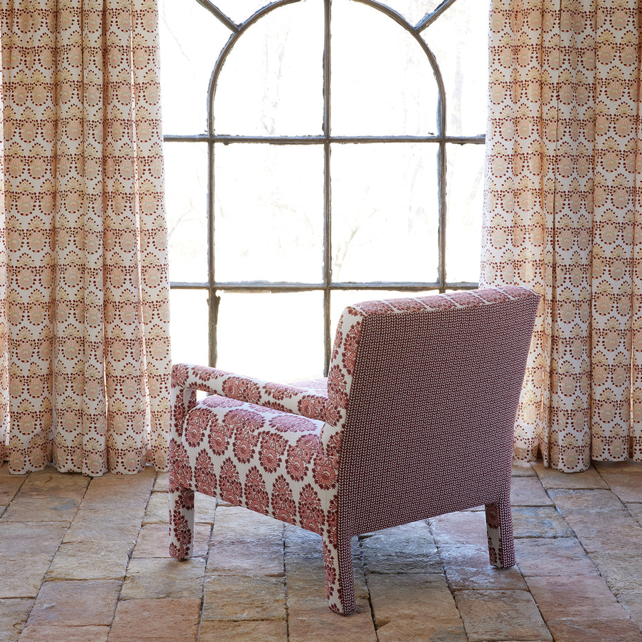 The Square Chair in Lanka Berry and Aleppo Berry by John Robshaw, featuring a striking red and white pattern reminiscent of a classic Kashmir block print, is placed in front of a large arched window framed by matching patterned curtains on a stone tile floor.