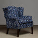 The John Robshaw Ashi Azure Woodruff Chair features elegant floral-patterned Ashi Azure fabric upholstery, dark wooden legs, and brass nailhead trim. Its classic wingback silhouette is enhanced by a sophisticated block print design and set against a plain gray background.