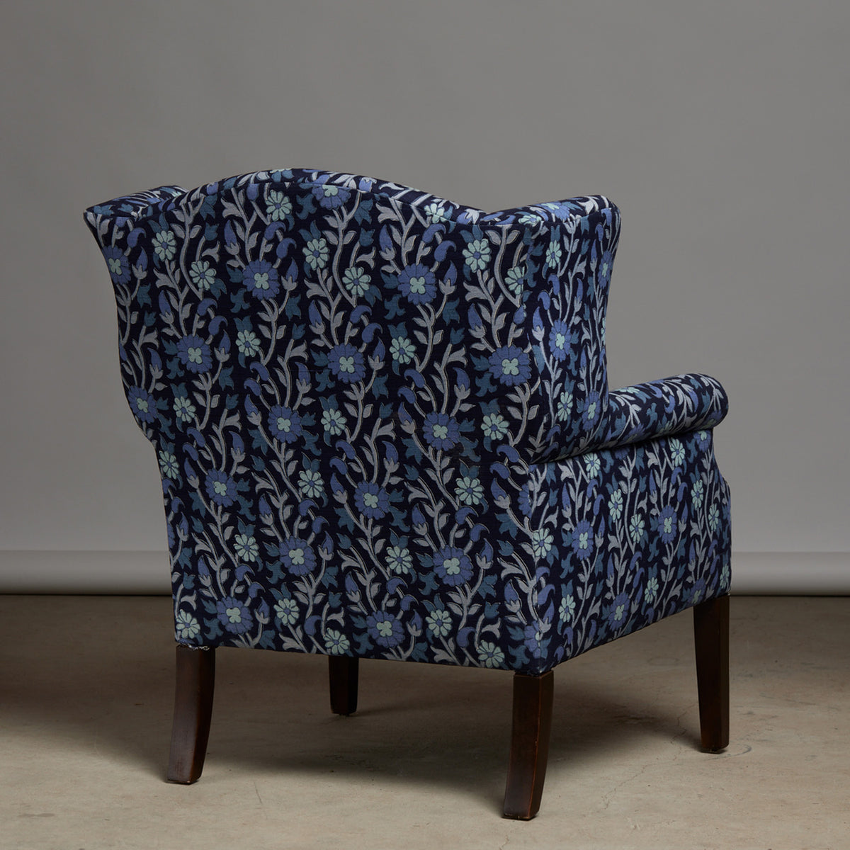 The Ashi Azure Woodruff Chair by John Robshaw is upholstered in elegant Ashi Azure fabric with traditional block print-inspired motifs, features dark wooden legs, and is shown facing away from the camera against a plain background.