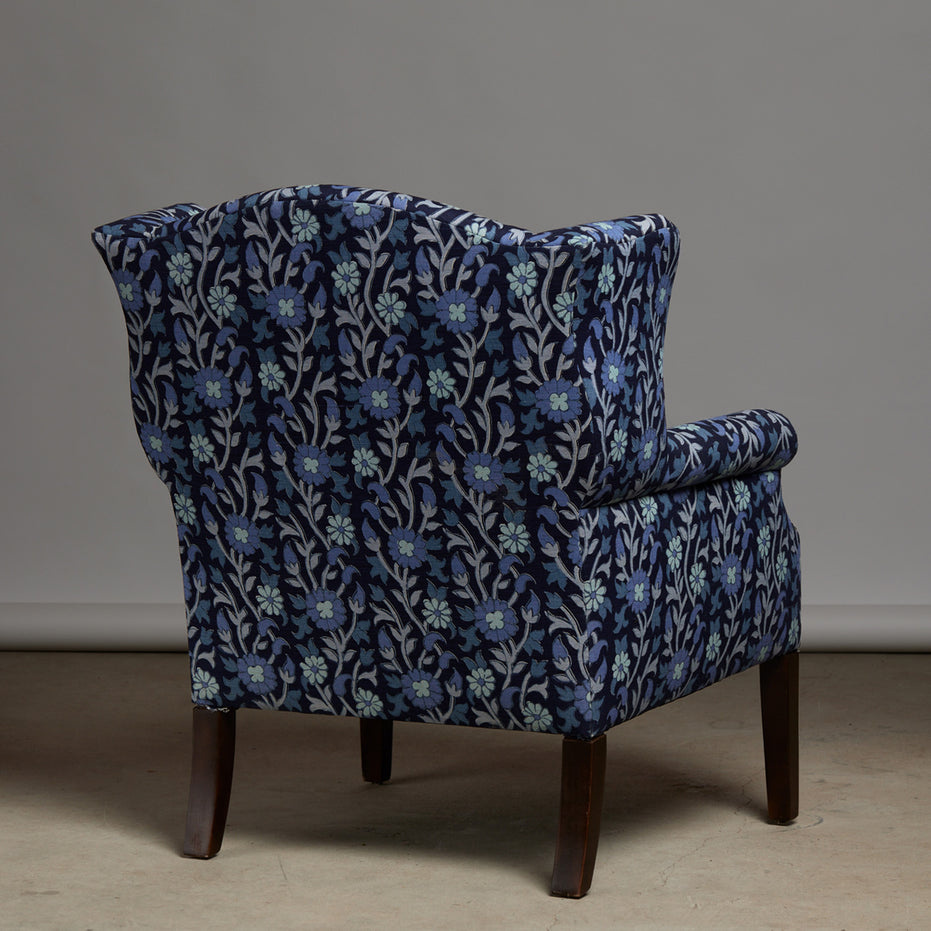 The Ashi Azure Woodruff Chair by John Robshaw is upholstered in elegant Ashi Azure fabric with traditional block print-inspired motifs, features dark wooden legs, and is shown facing away from the camera against a plain background.