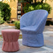 A chair upholstered in John Robshaw’s Balan Azure Fabric sits beside a red Sanganer clay print ottoman on a stone patio, surrounded by trees and bushes in the garden.
