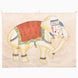 A hand-painted John Robshaw White Elephant Walking Tapestry featuring a walking elephant adorned with a floral red blanket, decorative headpiece, and ankle bells.