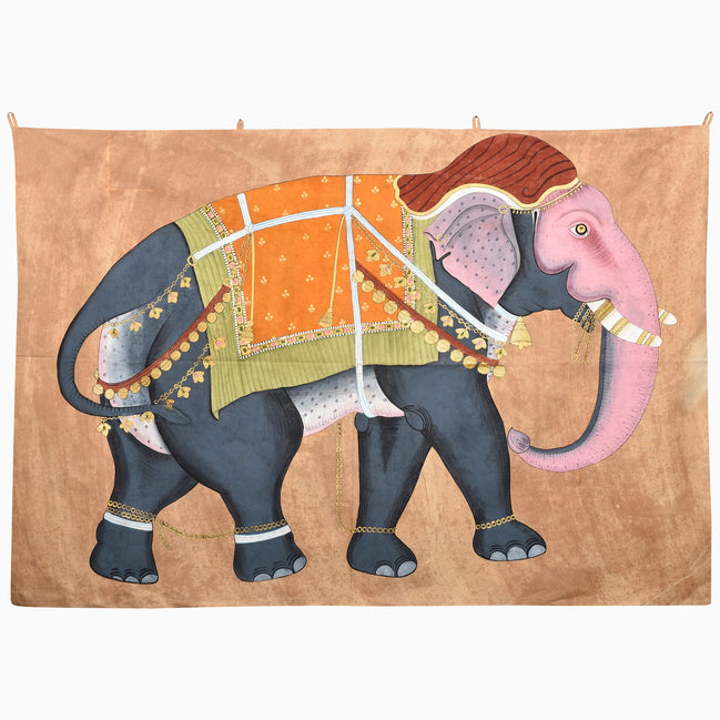 The On the Move Again Tapestry is a hand-painted piece depicting a stylized elephant with a pink head and trunk, wearing an orange and yellow embroidered jhool with gold tassels.