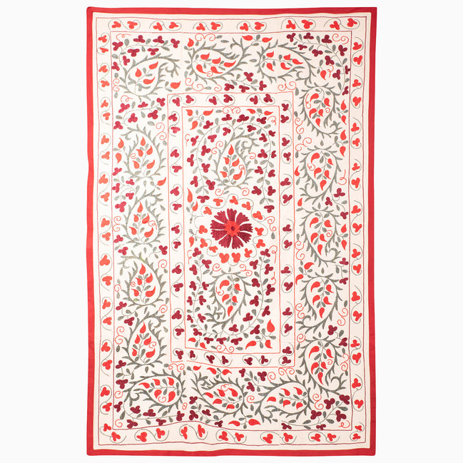 John Robshaw Come Along Then Suzani blanket in cream with a red border and an embroidered pattern of red and grey floral vines surrounding a central flower.