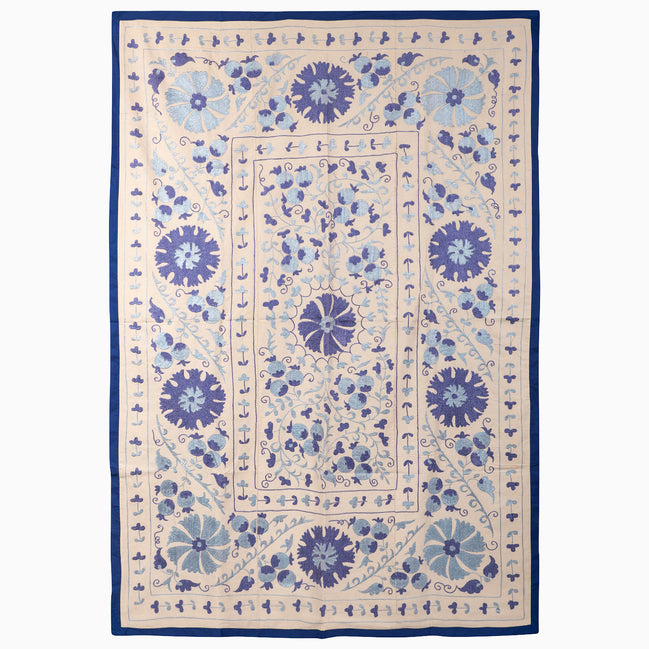 John Robshaw Open Water Suzani blanket, a rectangular vintage piece with blue floral and vine embroidery on a light background framed by a solid indigo fabric border.