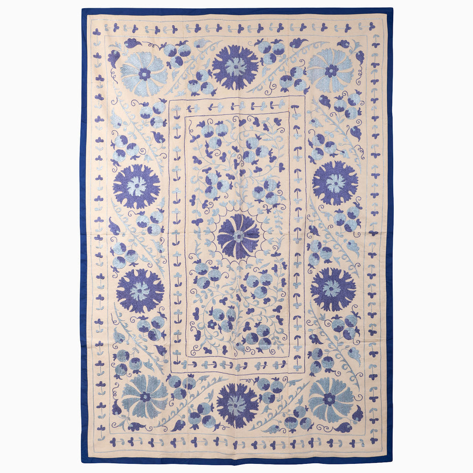 John Robshaw Open Water Suzani blanket, a rectangular vintage piece with blue floral and vine embroidery on a light background framed by a solid indigo fabric border.