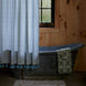 A metal bathtub with a patterned green towel, the John Robshaw Cala Sage Organic Shower Curtain in blue and white, and a wooden wall with a window in the background.