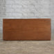 A Daksh Teak Table by John Robshaw sits on a concrete floor, set against a white brick wall and evoking the vintage charm and timeless appeal of handcrafted furniture.