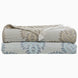 Two folded patterned blankets, one brown and one blue, stacked on top of each other. The top blanket, the Dasati Sand Throw from John Robshaw, is crafted from stonewashed cotton and also features fringe detailing.