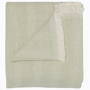 The Lavanya Sage Throw by John Robshaw is a folded, light cotton blanket featuring a subtle herringbone pattern and one fringed edge.