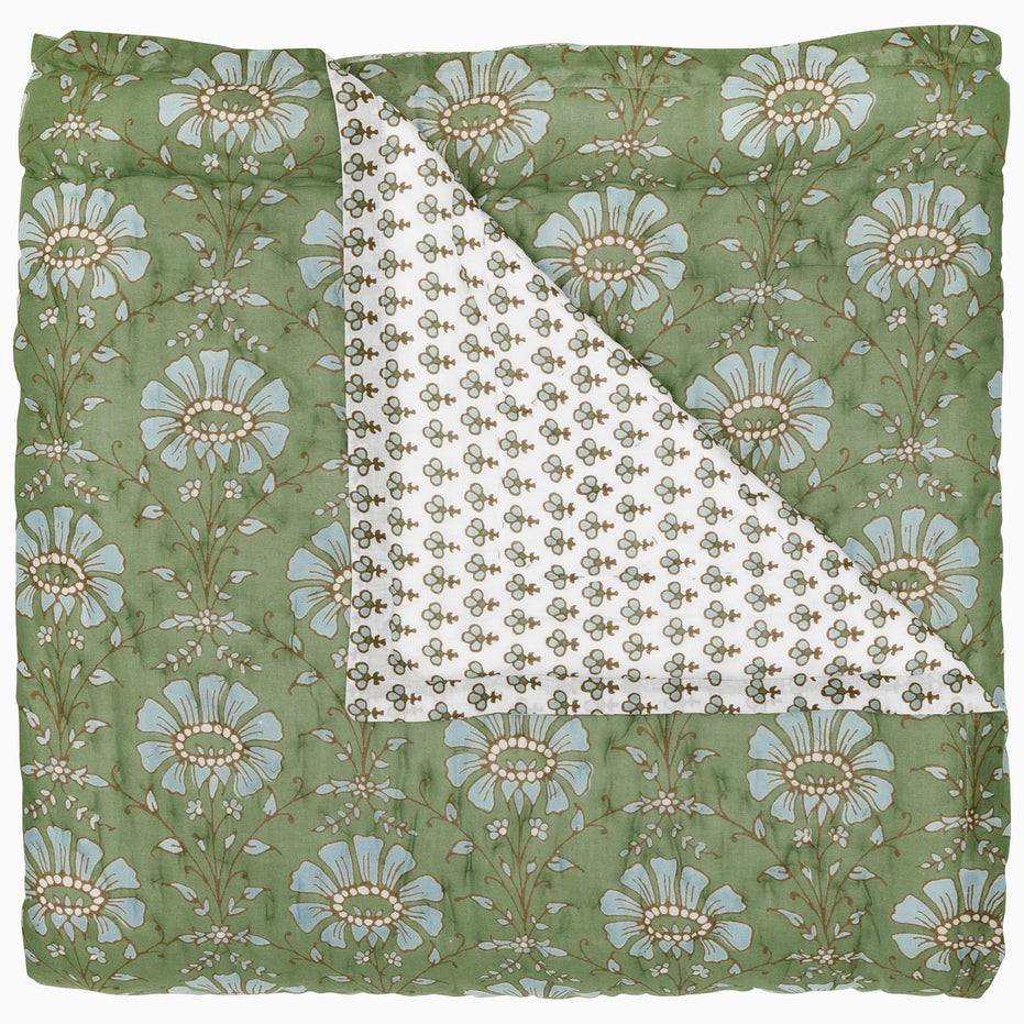 The Jeeva Sage Quilt by John Robshaw, featuring a charming green floral pattern and hand-quilted craftsmanship, showcases a folded corner that reveals a white fabric underside adorned with a delicate smaller floral design, evoking the charm of a spring meadow.