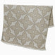 A John Robshaw Dasati Sand Throw, featuring a beige fabric with an intricate leaf-like woven design and fringed edging, draped open against a plain background.