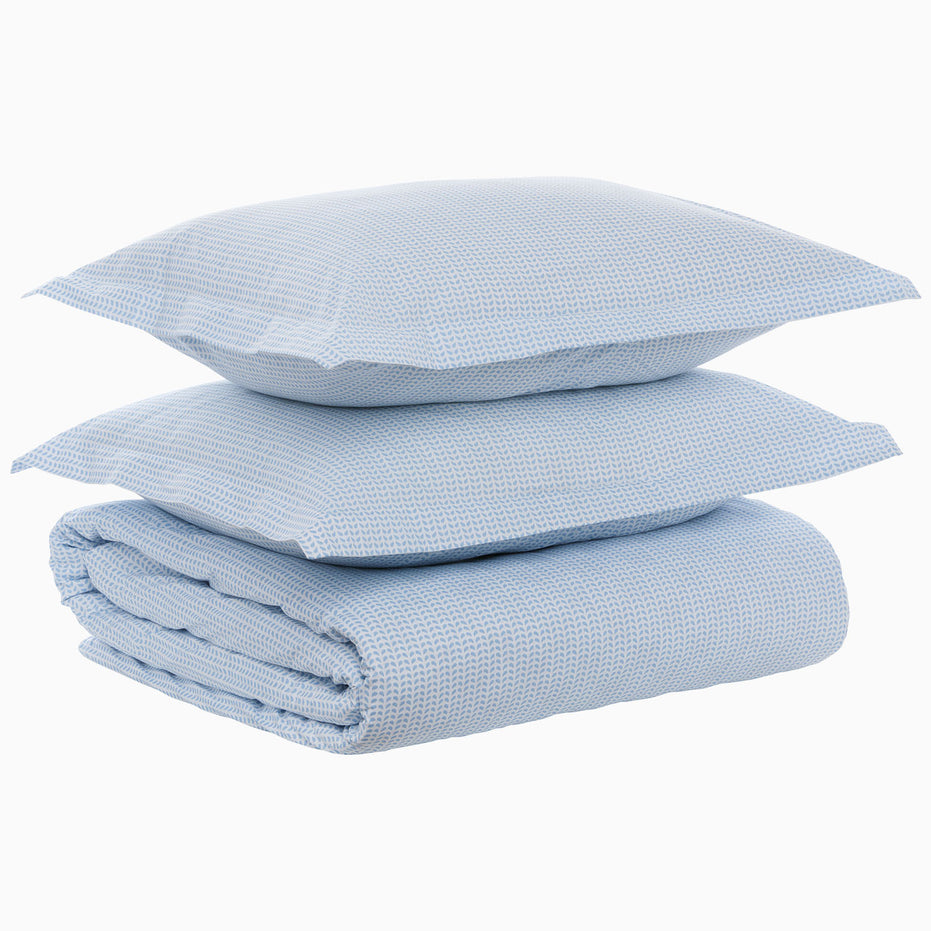 A folded Cinde Light Indigo Organic Duvet and two matching pillows stacked on top of each other against a white background, all crafted from organic cotton duvet material with a 200 thread count percale finish by John Robshaw.
