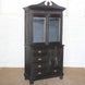 The Rajan Wooden Cabinet by John Robshaw features mirrored double doors on top, four drawers, and two small lower doors for versatile storage; its dark wood finish and round legs add elegance as it stands atop a woven floor mat.