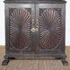 The Mayura Wooden Cabinet by John Robshaw features two ornate, carved sunburst panels with a radial pattern and decorative corners. This dark wooden cabinet sits on clawed feet and is displayed on a woven mat.