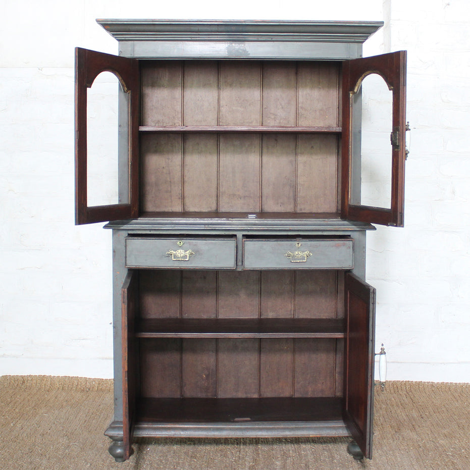 The Revati Wooden Cabinet by John Robshaw showcases arched glass doors, two drawers, and lower cabinet doors that open to reveal spacious empty shelves inside.