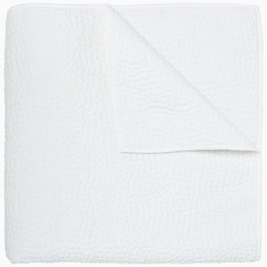 An Organic Hand Stitched White Quilt by John Robshaw folded on top of a white surface.