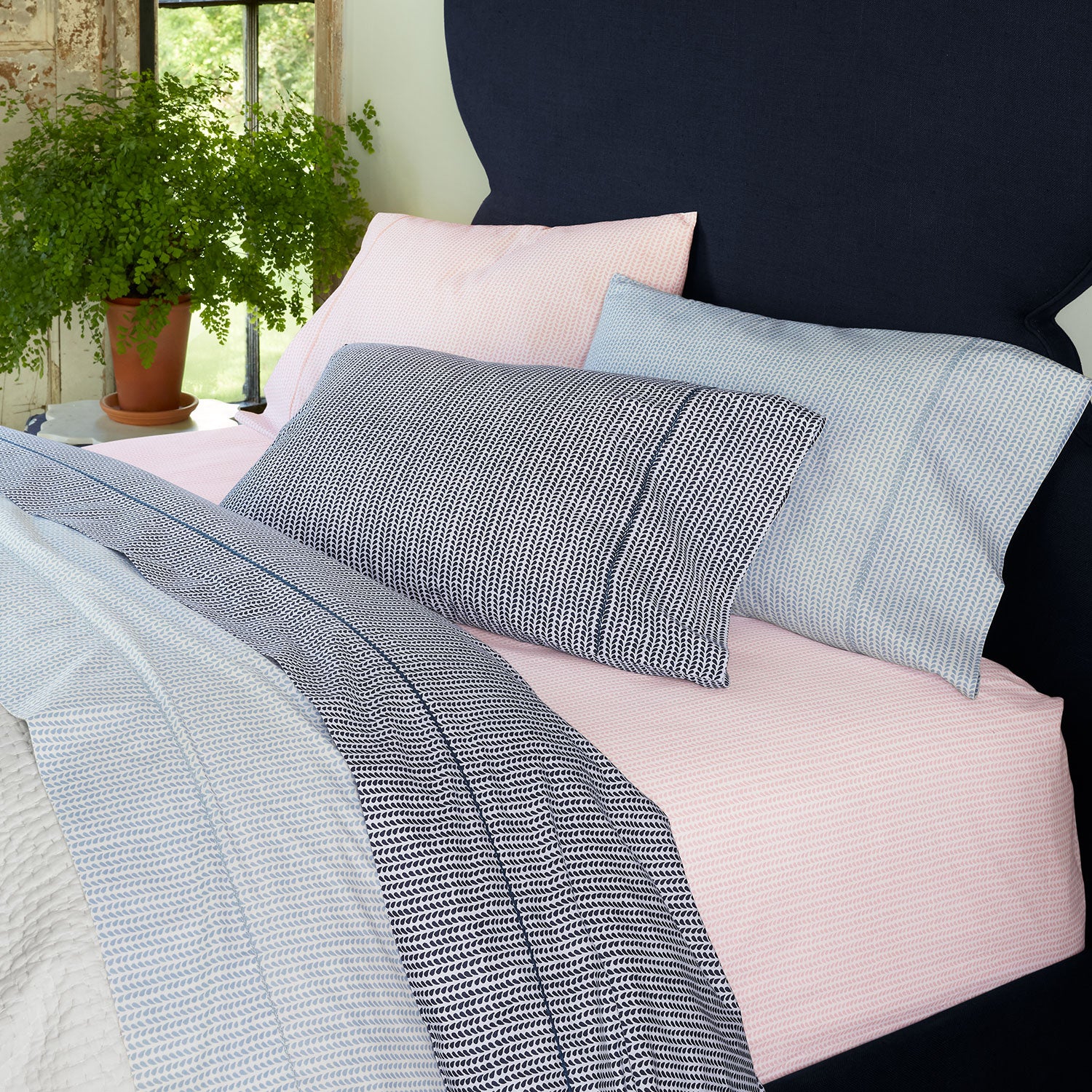 A 100% cotton percale bed with blue, pink, and white bedding, including a John Robshaw Cinde Light Indigo Organic Sheet Set.