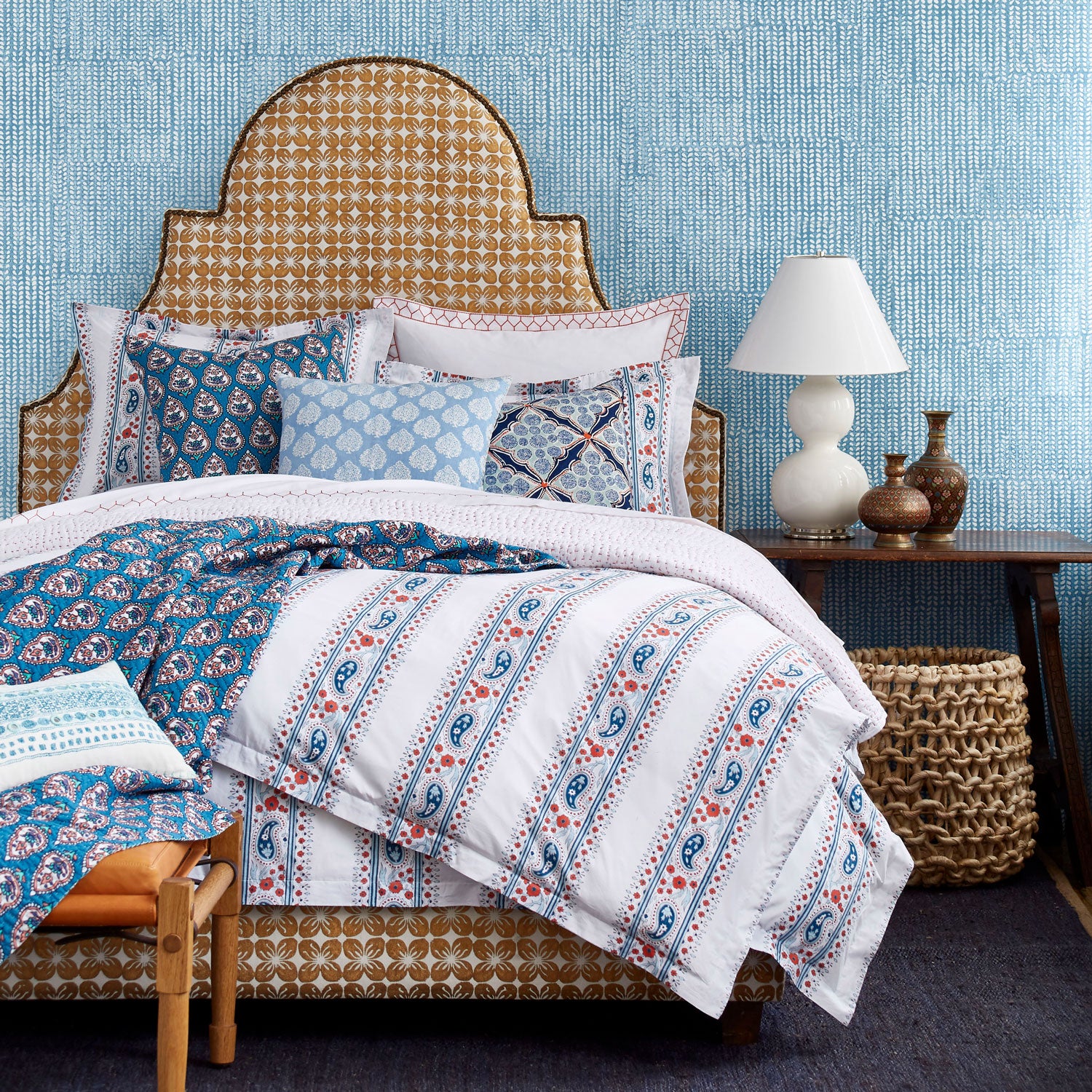 A Custom Dara Bed with blue and white bedding and a John Robshaw wicker basket available for white glove delivery.